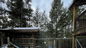 A snowy outdoor area with a wooden deck, a slide, and a swing set.