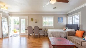 A spacious room with a wooden floor, a bed, a sofa, a dining table with chairs, and a ceiling fan. - Casa Alquimia-Chula Vista Home, Private patio. (Chula Vista)
