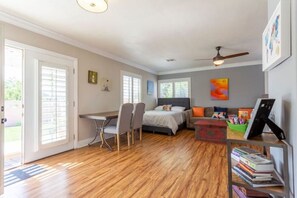 A bedroom with a bed, a desk, and a chair. There is a bookshelf with books and a painting on the wall.