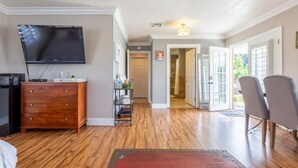 A living room with a flat-screen TV, wooden flooring, a red rug, and a dining area with chairs. - Casa Alquimia-Chula Vista Home, Private patio. (Chula Vista)