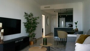 Una sala moderna con un televisor de pantalla plana, un sofá, una mesa de centro y una zona de comedor con sillas.