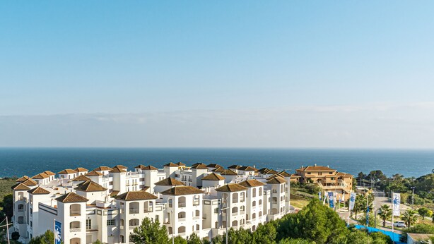 Un hotel costero con varias edificaciones blancas, una piscina grande y vistas al mar.