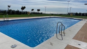 Una piscina rectangular con una superficie de agua azul cristalina, rodeada por un solárium de azulejos.