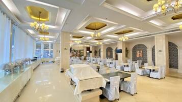 A spacious restaurant with multiple tables and chairs, a long counter with a glass display, and decorative lighting.