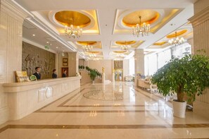 A hotel lobby with a reception desk, chandeliers, and a large potted plant. - Vienna Hotel (Guilin)