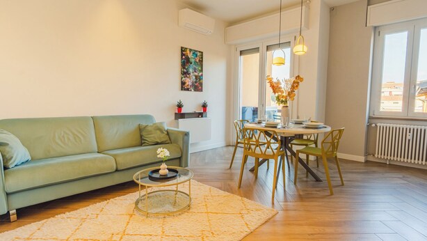 Ein Wohnzimmer mit einem grünen Sofa, einem runden Esstisch mit gelben Stühlen und einer weißen Heizung.