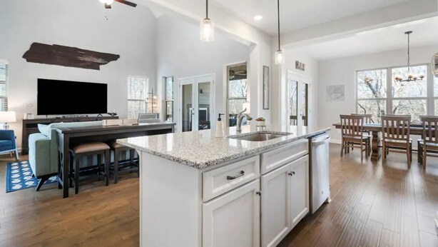 A modern kitchen with a central island, white cabinetry, and a dining area with wooden chairs and a table. - Tims Ford Lake Retreat - The Got-Away (Tullahoma)