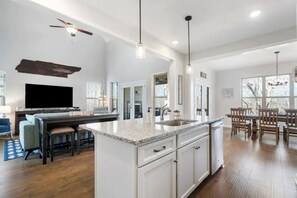 Une cuisine moderne dotée d’un îlot central, de meubles blancs et d’un coin repas avec des chaises et une table en bois.