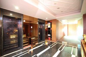 Un vestíbul d'hotel amb un sòl de marbre polit, una taula de recepció i un panell d'informació fixat a la paret.