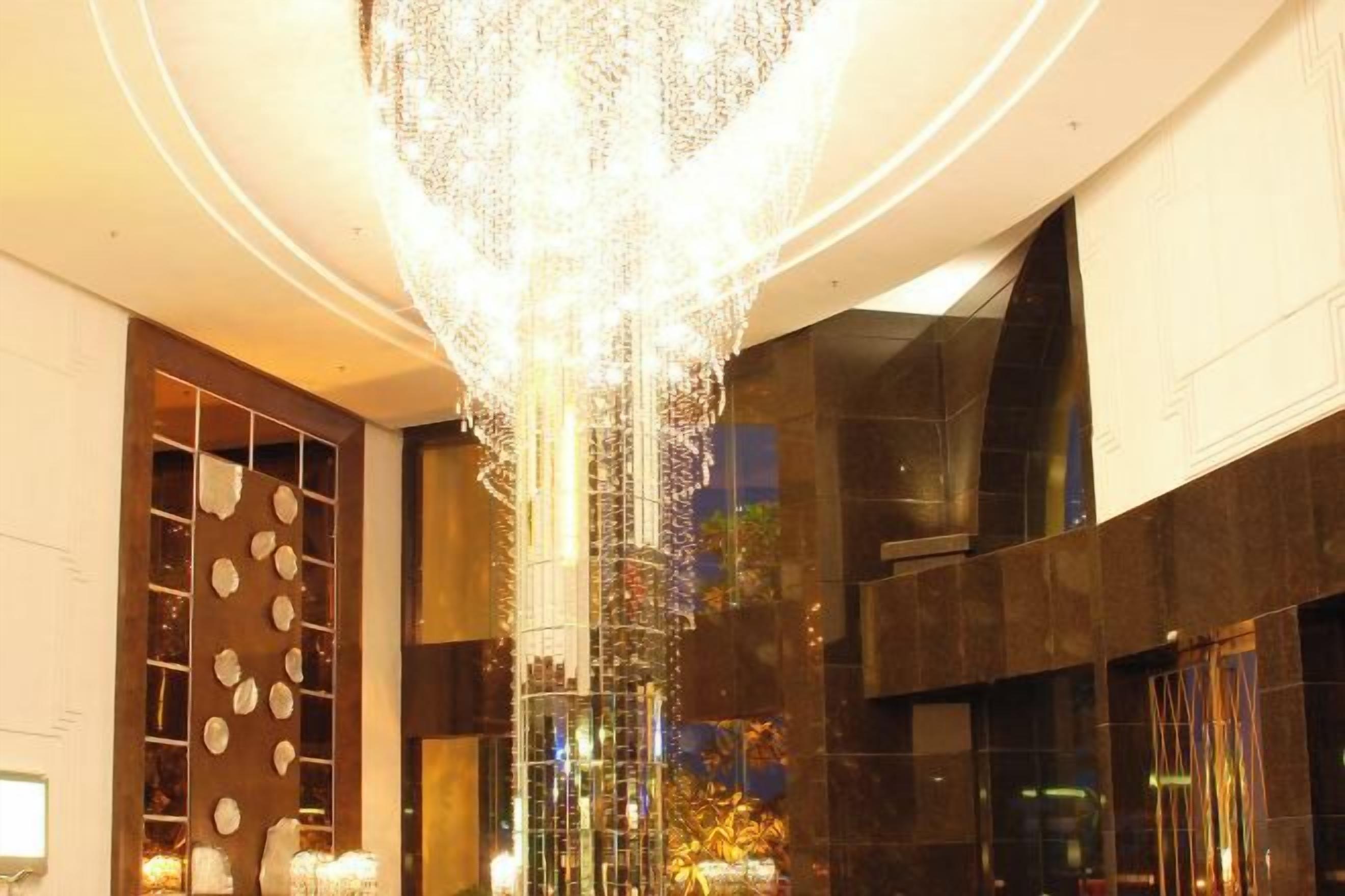 Un interior moderno con una lámpara central, superficies reflectantes y un diseño de pared geométrico.