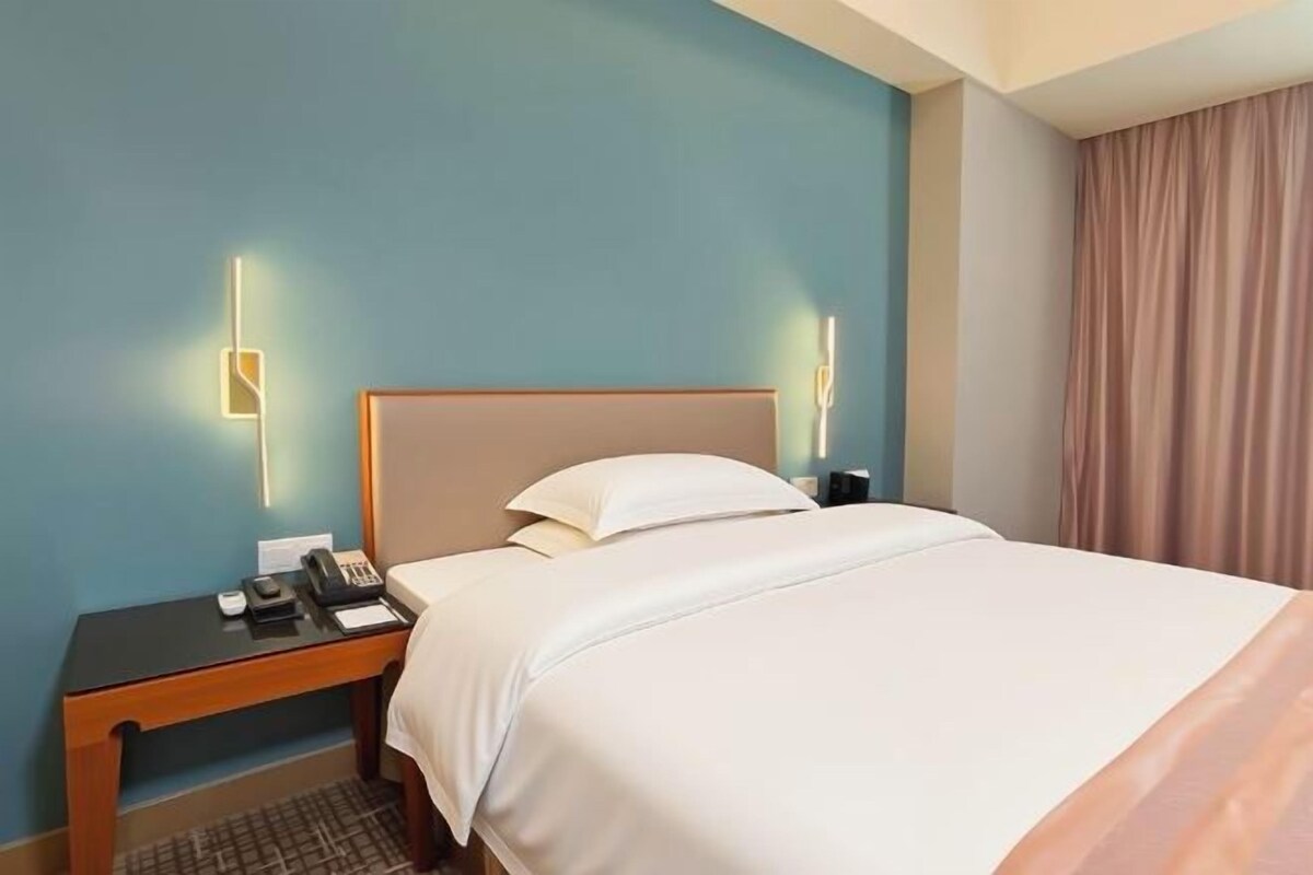 Una habitación de hotel con cama, mesita de noche, lámpara y cortinas.