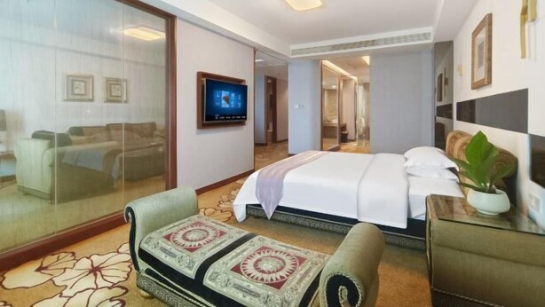 Quarto de hotel com cama, sofá, televisão e porta de vidro que dá para uma varanda.