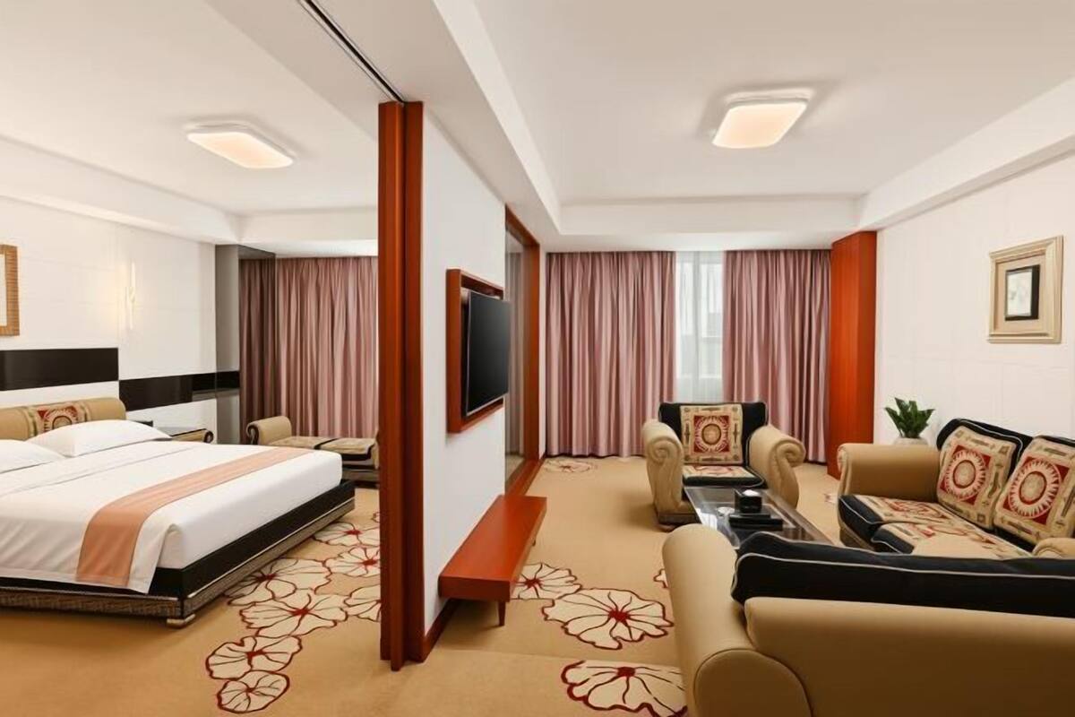 A hotel room with a bed, a sofa, a TV, and a carpet with floral patterns.