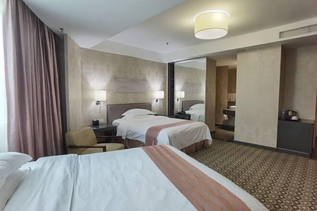 A hotel room with two beds, a desk, a chair, a mirror, and a carpeted floor.