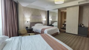 Quarto de hotel com duas camas, uma escrivaninha, uma cadeira, um espelho e piso coberto de carpete.