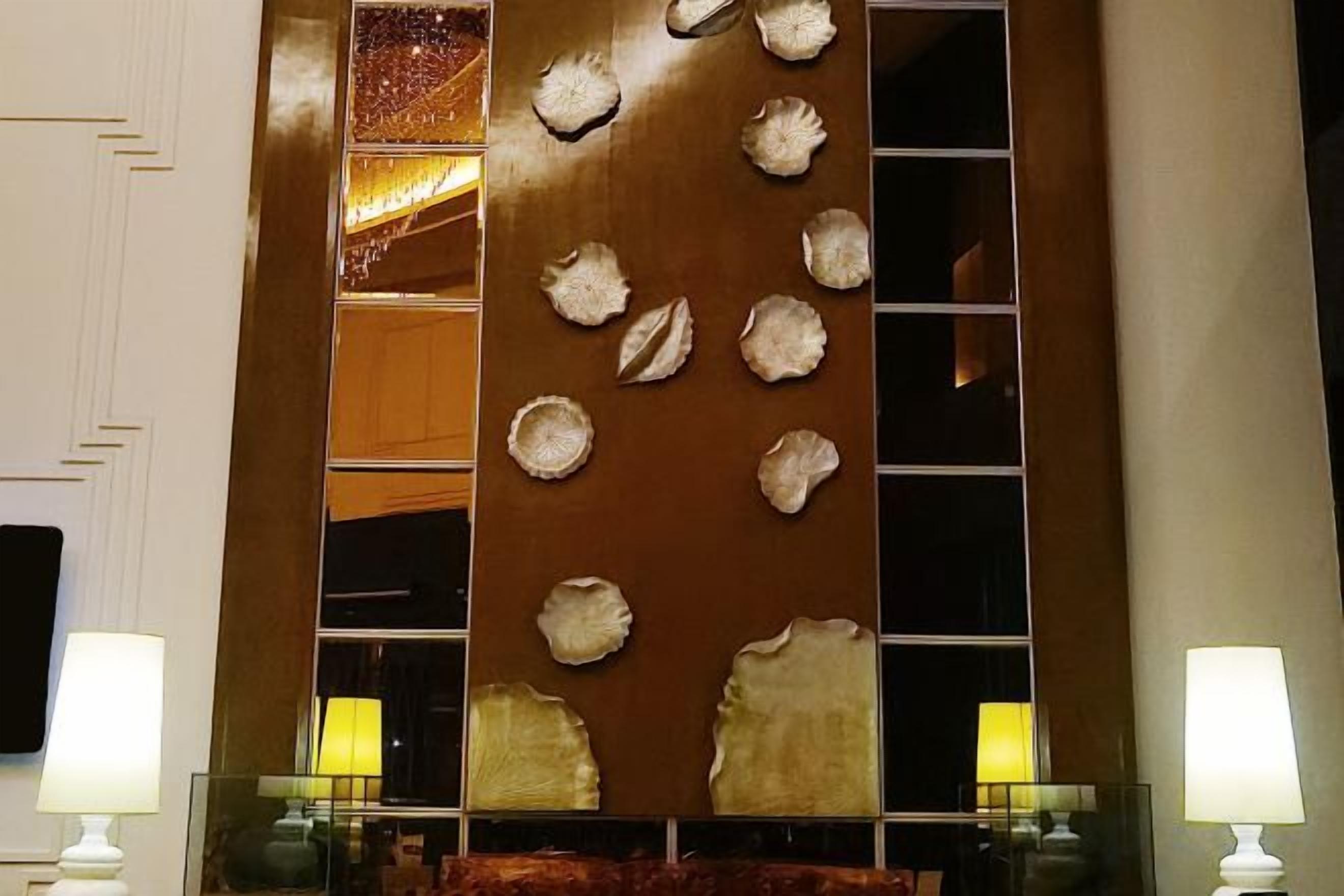 A wall with a decorative panel and a mirror. There are two lamps on either side of the mirror.