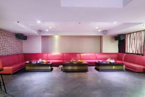 A spacious room with a red sectional sofa, two coffee tables, and a large screen. - Tianying Hotel (Dongguan)