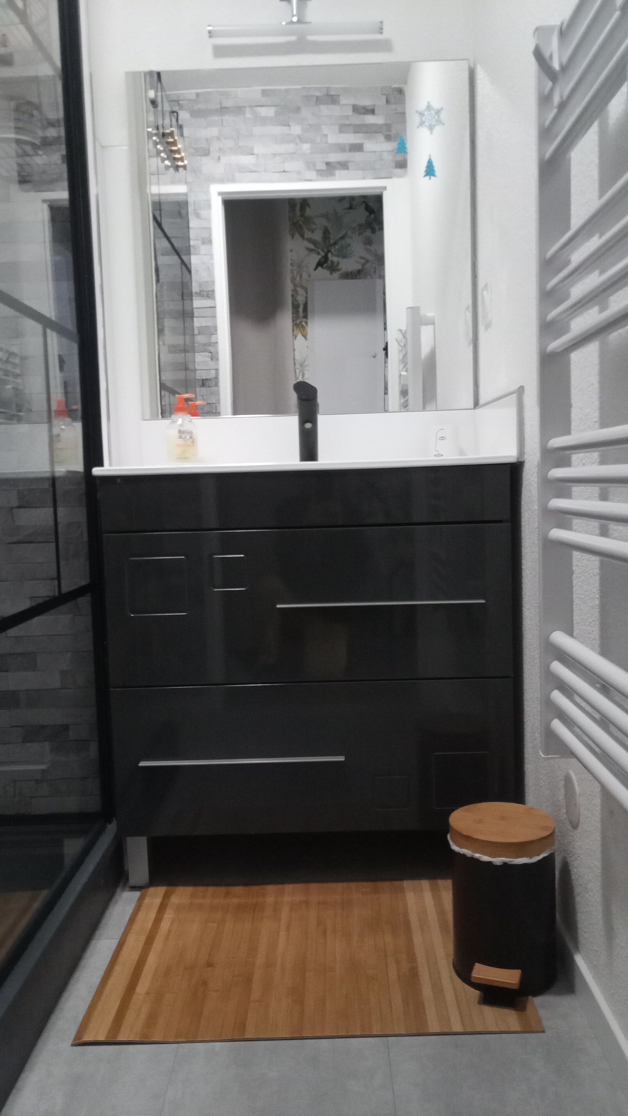 A modern bathroom with a black vanity, a mirror, and a small wooden stool.