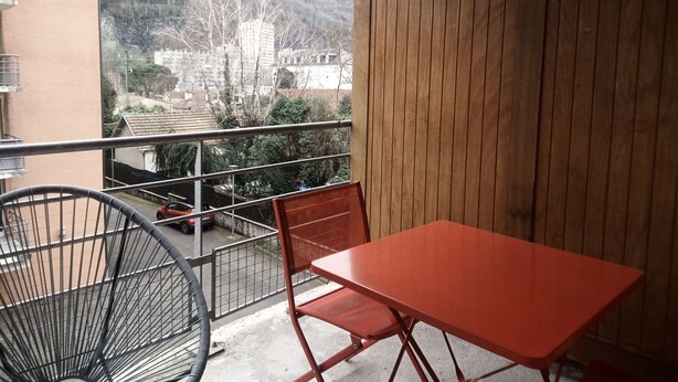 A balcony with a red table and chairs, a view of a mountain and buildings in the background. - Quiet, well-located 1 bed 140, secure covered parking  (Lourdes)