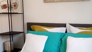 A bed with a colorful bedspread, a black metal shelf unit, and a painting of birds on the wall. - Quiet, well-located 1 bed 140, secure covered parking  (Lourdes)