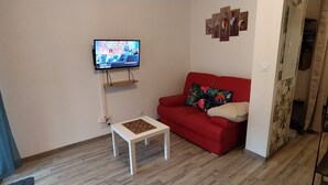 A living room with a red sofa, a small white table, a TV mounted on the wall, and a decorative wall piece. - Quiet, well-located 1 bed 140, secure covered parking  (Lourdes)