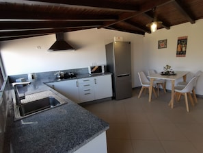 A kitchen with a stainless steel refrigerator, a microwave, a stove, and a sink. There is a dining table with white chairs.
