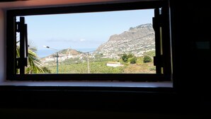 Ein Fenster mit Blick auf eine gebirgige Landschaft, einen klaren Himmel und ein weit entferntes Gewässer.