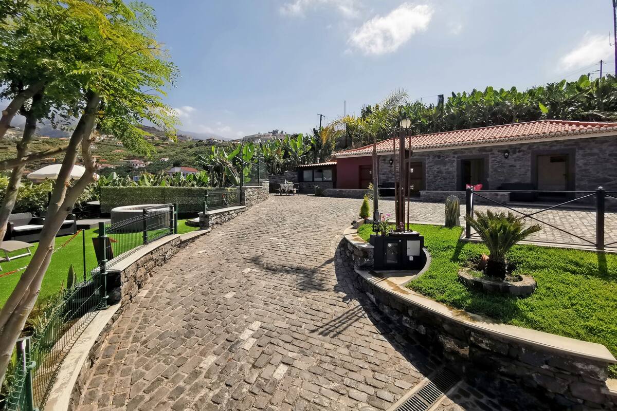 A cobblestone courtyard with a stone wall, a small garden with a lamp post, and a building with a red-tiled roof.