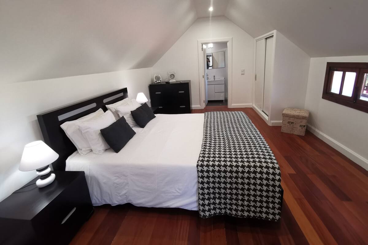 A bedroom with a large bed, a nightstand, a dresser, a walk-in closet, and a window.