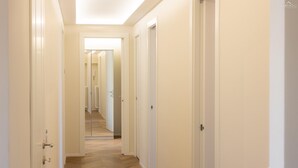 A hallway with white walls and wooden flooring, leading to multiple doors. - Aurelia Sunset Penthouse (Rome)
