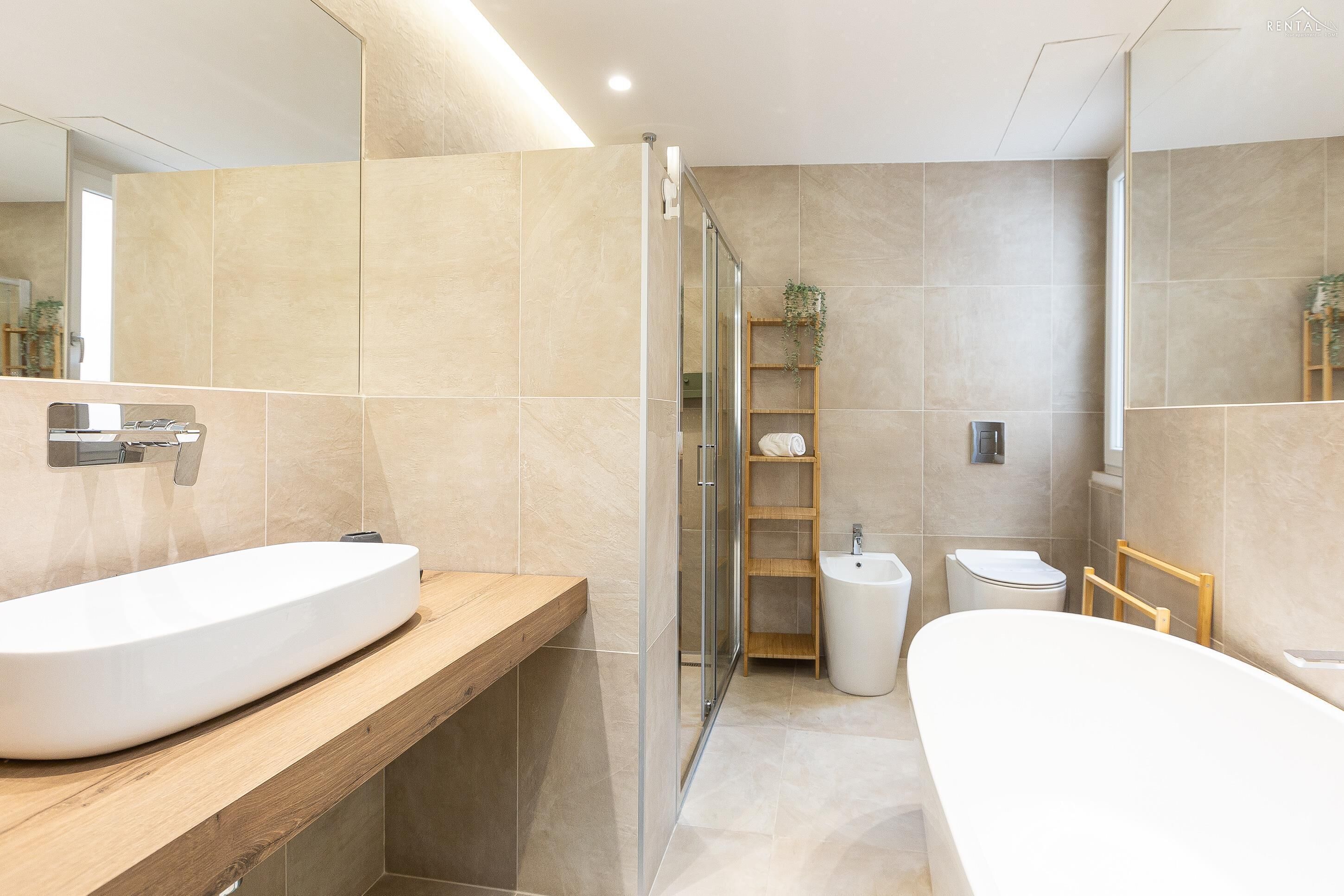 A modern bathroom with a large white sink, a glass shower enclosure, a toilet, and a bathtub.