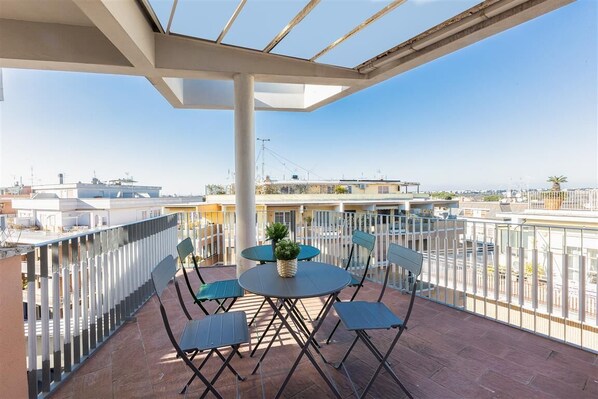 A balcony with a table and chairs, a potted plant, and a view of buildings in the distance.