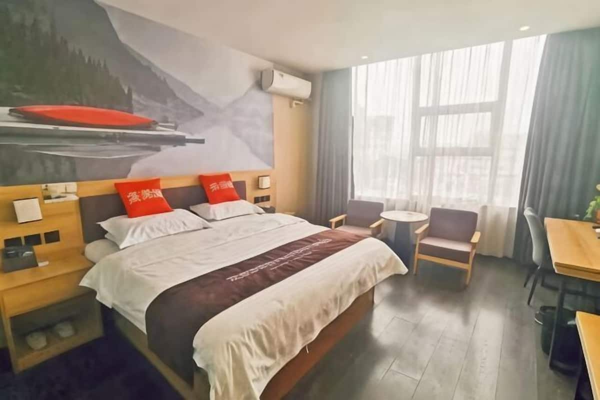 A hotel room with a large bed, a desk, a chair, a small table, and a window with curtains.