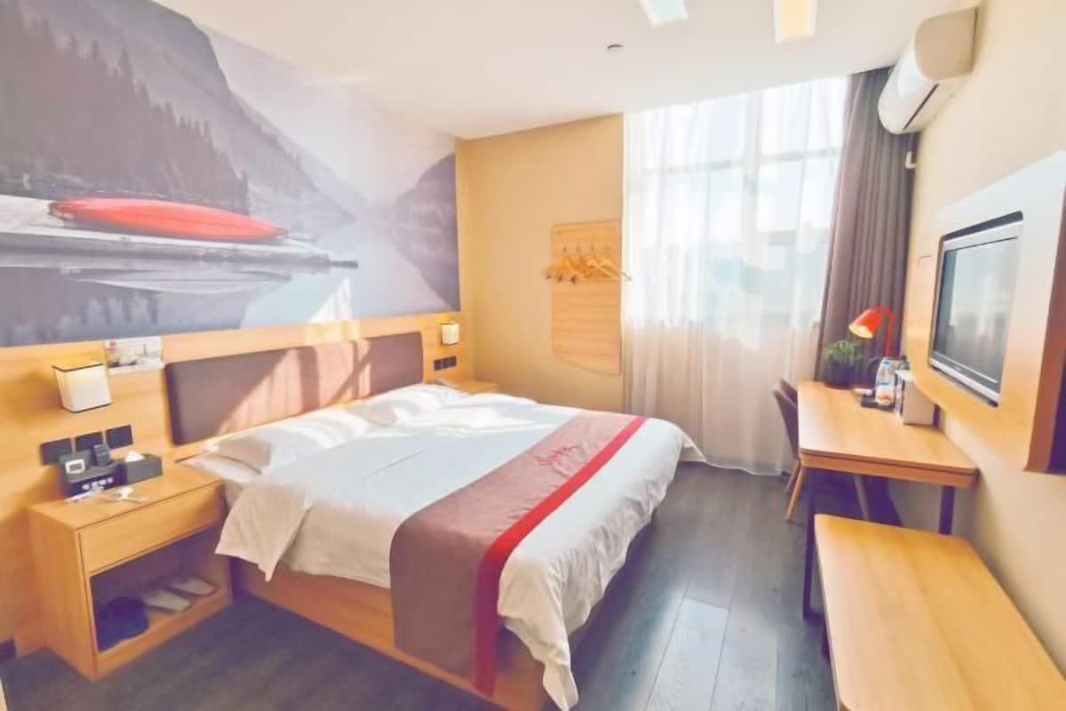 A hotel room with a bed, bedside tables, a desk, a TV, and a mural on the wall.