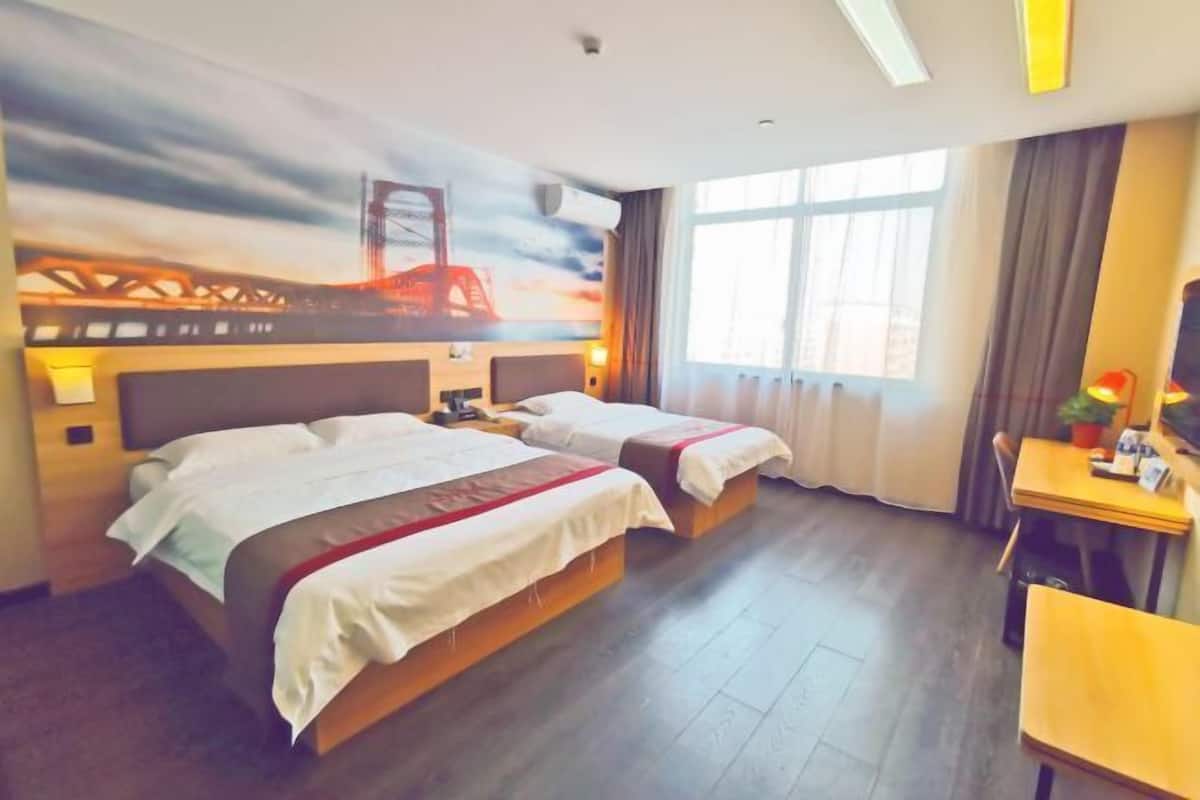 A hotel room with two beds, a desk, and a large window.