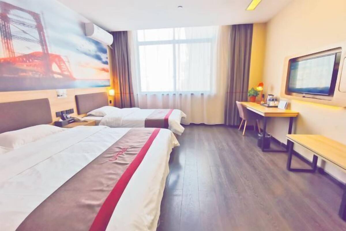 A hotel room with two beds, a desk, a TV, and a large window with curtains.