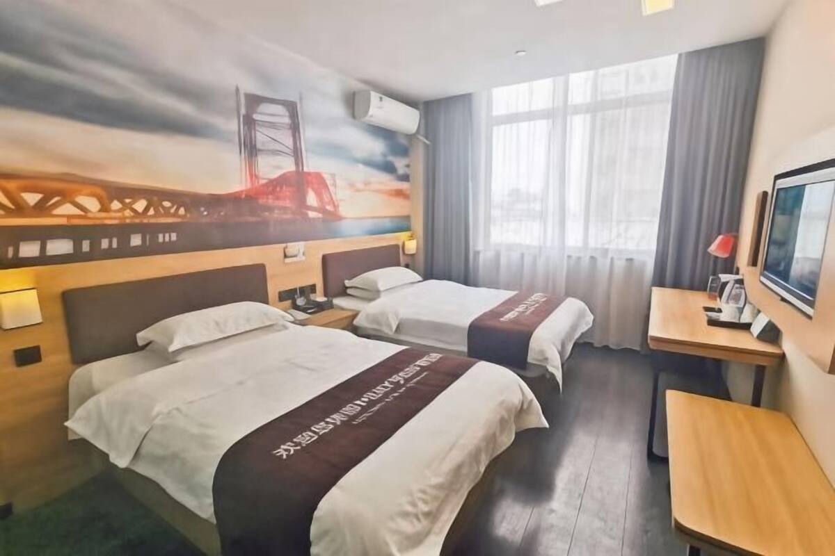 A hotel room with two beds, a desk, a TV, and a mural of a bridge.