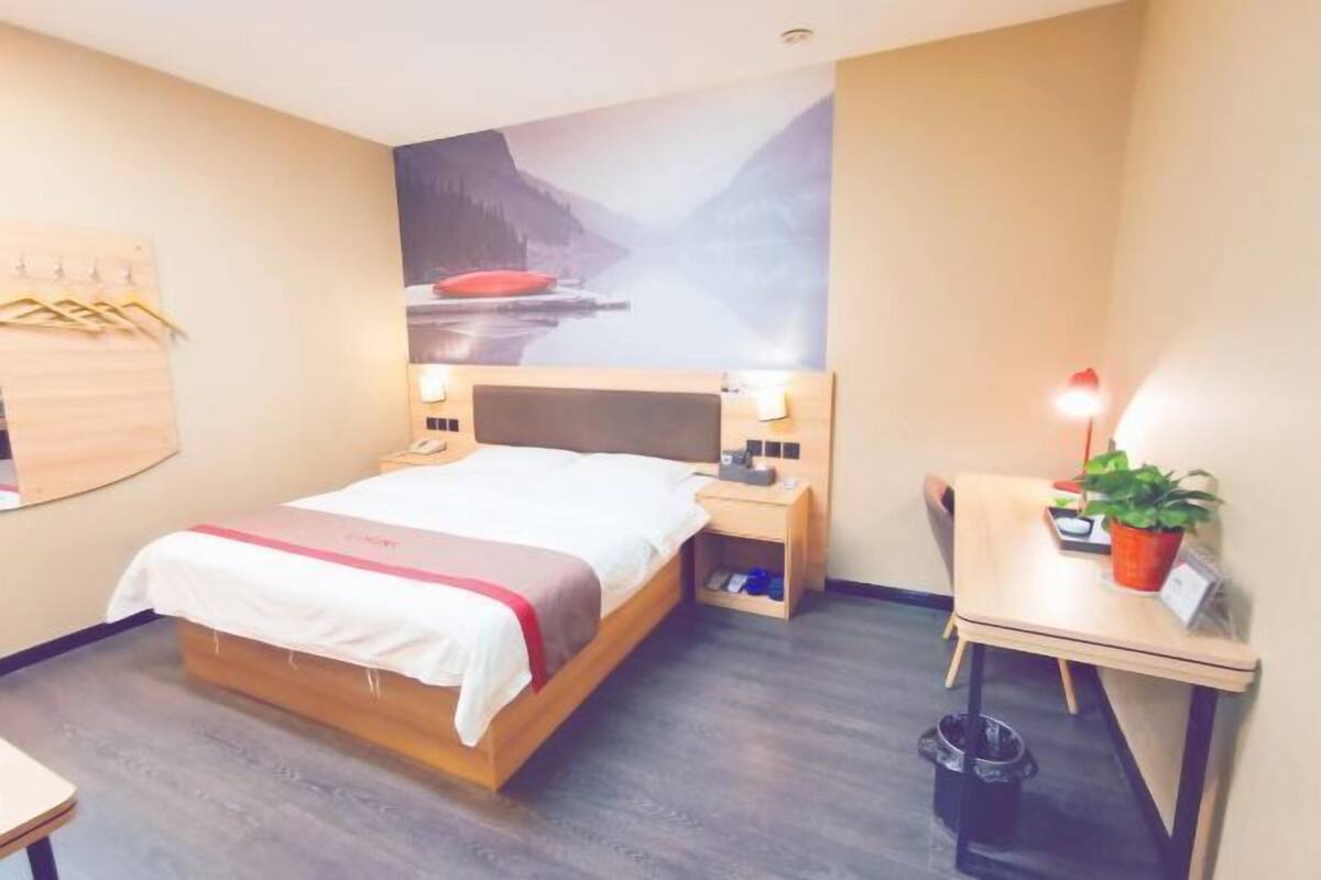 A hotel room with a bed, bedside table, lamp, and a small desk with a chair.