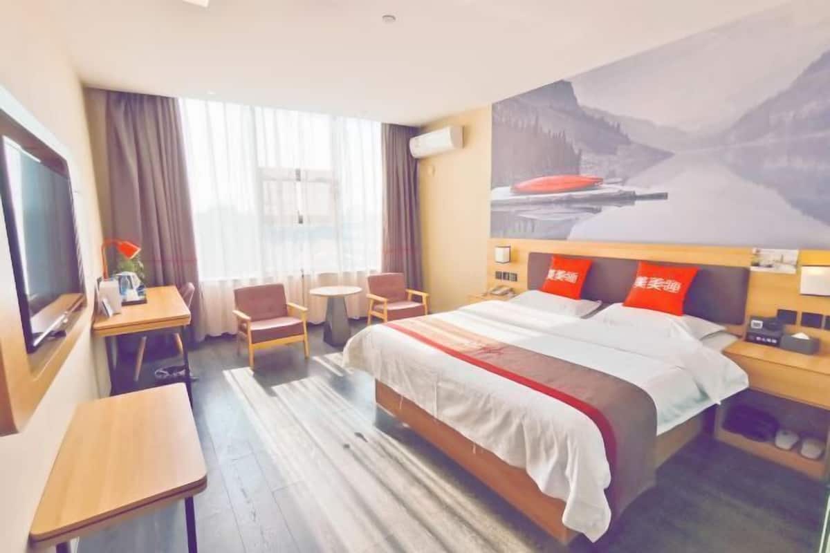 A hotel room with a bed, a desk, a chair, a TV, and a painting on the wall.