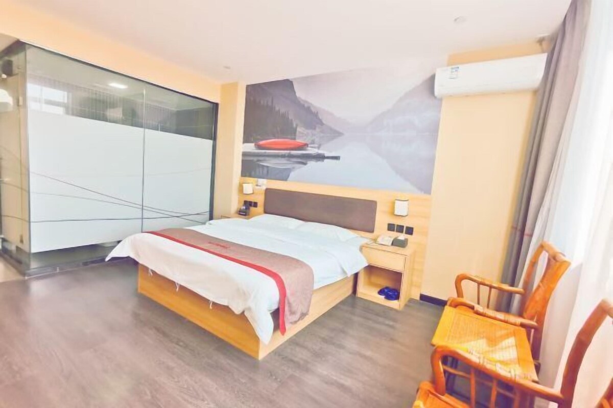 Een hotelkamer met een bed, nachtkastje, stoel en een groot muurschilderij.