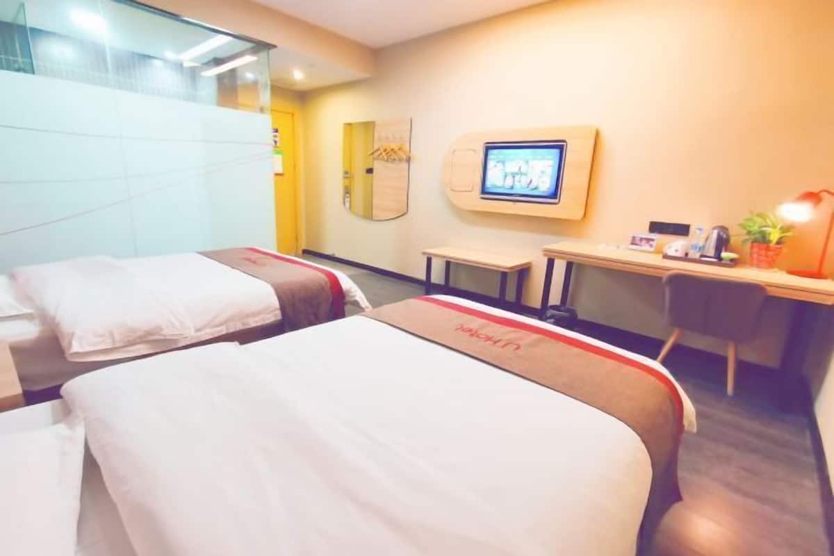 A hotel room with two beds, a desk, a television, and a small table with a plant.