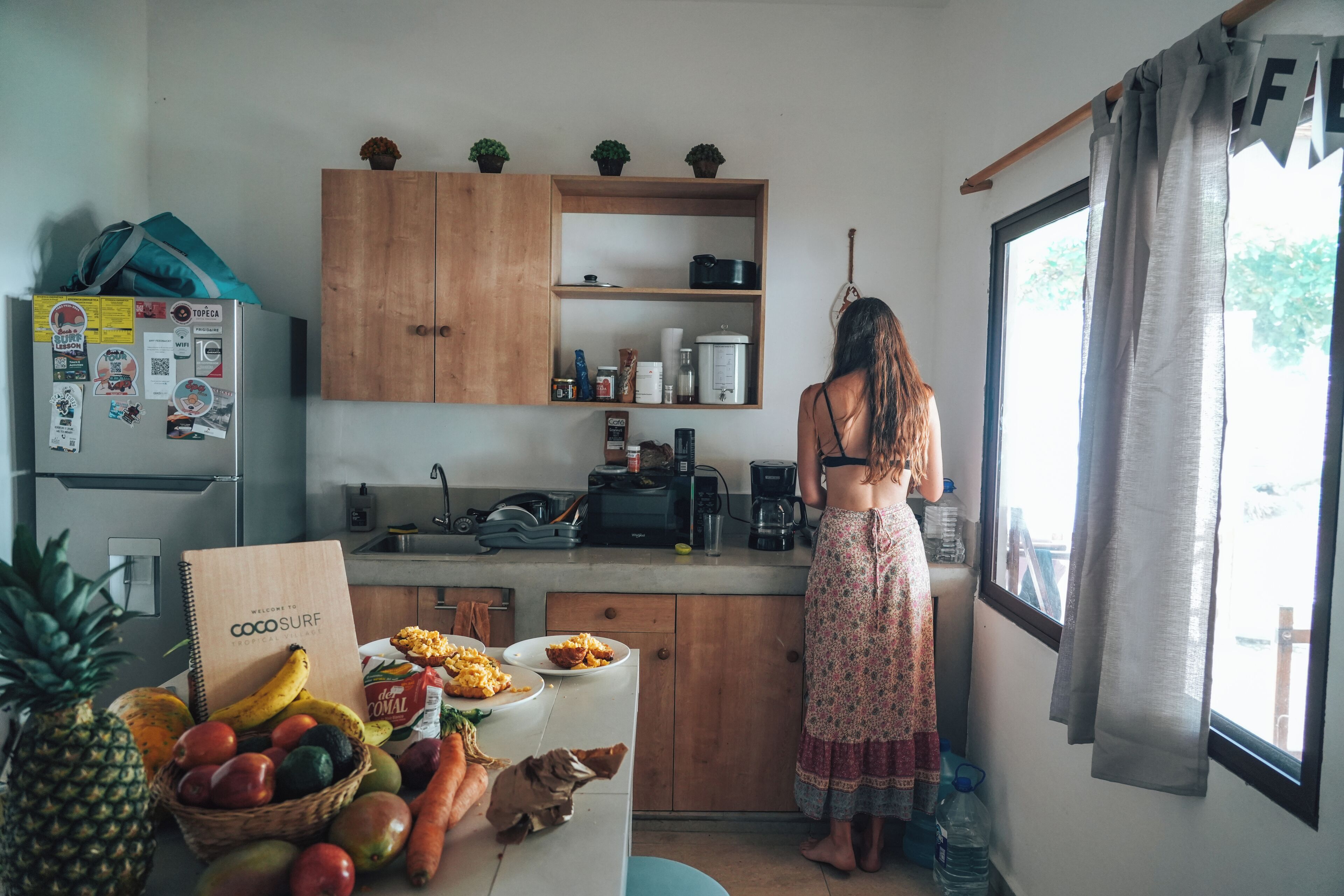 A kitchen with wooden cabinets, a refrigerator, and a window with curtains.