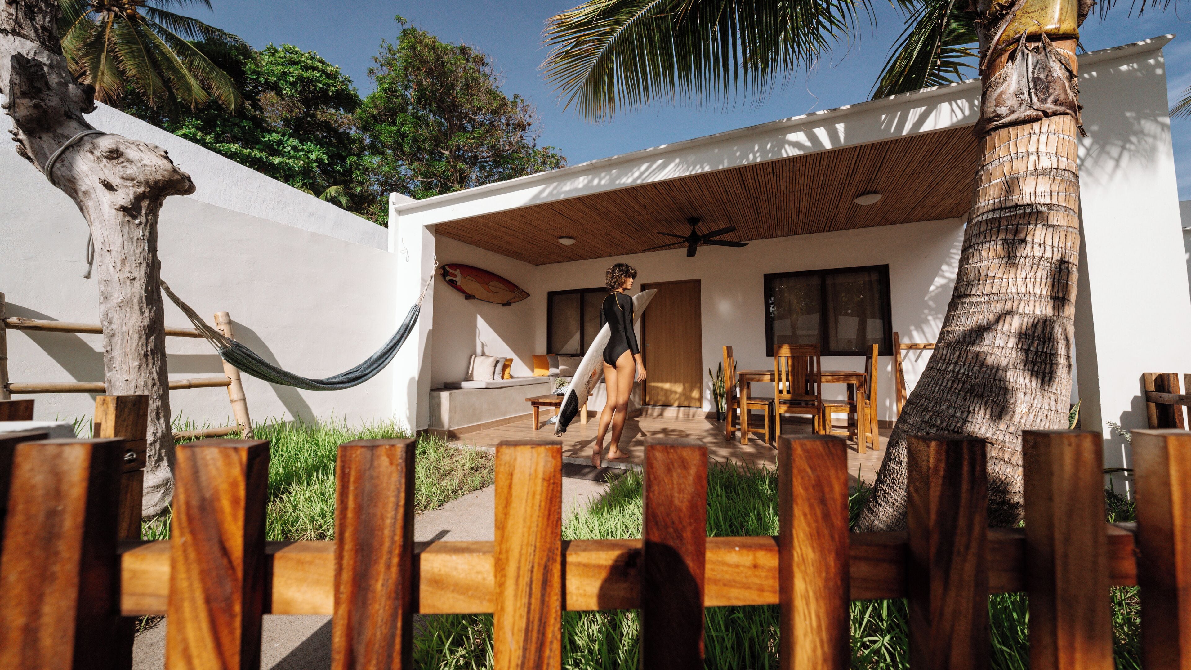 Un edificio moderno con una terraza de madera, una hamaca y una tabla de surf.