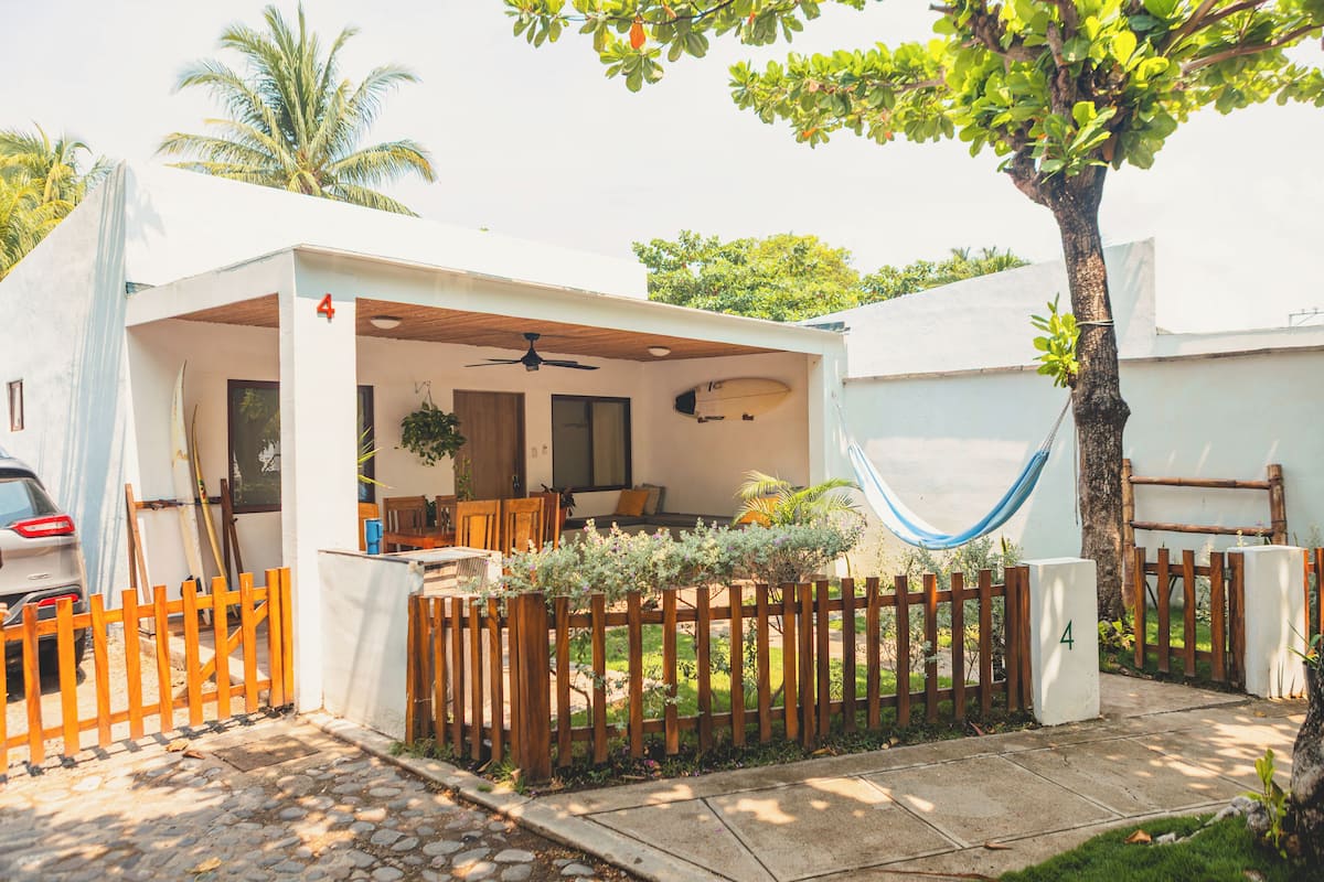 A house with a covered patio, a hammock, and a wooden fence.