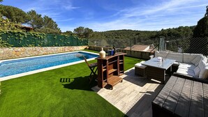 Ein Garten mit Swimmingpool, einem Holztisch und einer Rattan-Couch.