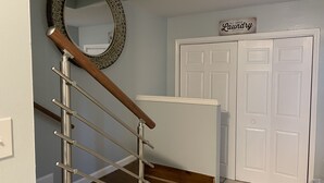 Un escalier avec une rampe en bois et des balustrades en métal, un miroir et un panneau indiquant qu’il s’agit d’une laverie en libre-service.