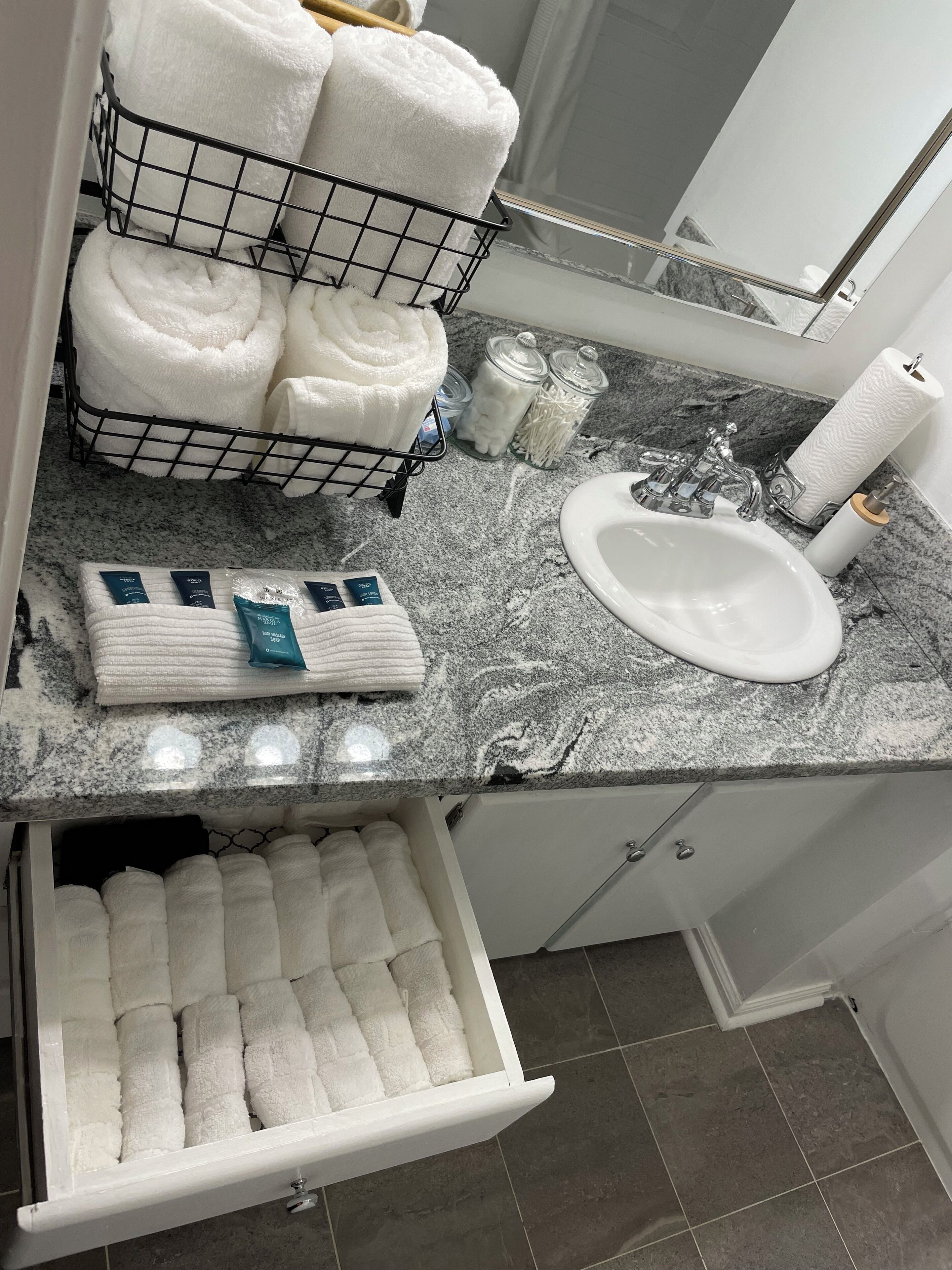 Un baño con encimera de mármol, un lavabo, un perchero para toallas y un cajón con toallas dobladas cuidadosamente.