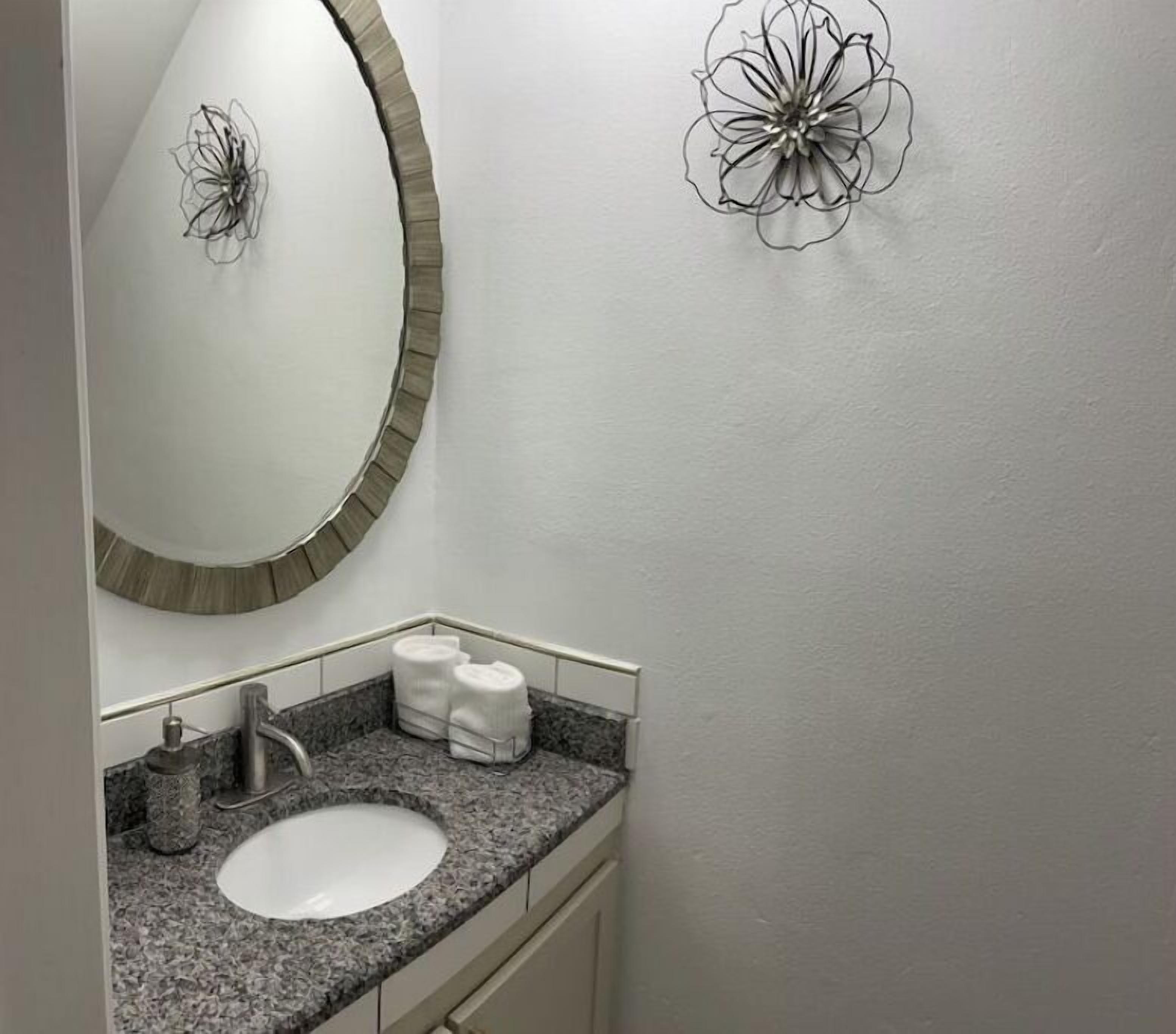 A bathroom with a granite countertop, a white sink, a mirror with a wooden frame, and two wall-mounted towel racks.