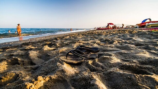 Une paire de tongs sur une plage de sable, avec des bateaux et des personnes en arrière-plan.