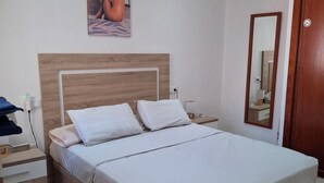 Une chambre à coucher avec une tête de lit en bois, un lit recouvert de draps blancs, une table de chevet avec une lampe et un ventilateur de plafond.